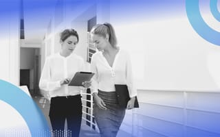 HRBP image of two women walking down a corridor. One holds an iPad and points to something on the screen, the other looks over her shoulder.