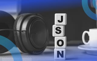 JSON image of a pair of headphones and a cup of coffee on a desk. In between them we see a pair of blocks stacked vertically spelling out J S O N