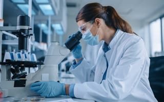 A woman in white lab coat looks into a microscope.