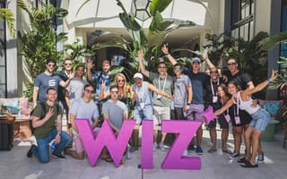 The Wiz team is pictured around a pink sculpture of the company logo.
