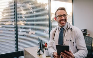 A male doctor smiles while looking off camera and holds a tablet