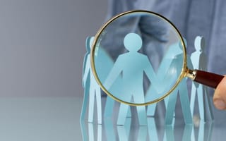 A magnifying glass hovering over small paper cutouts of people.