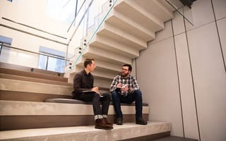 Two employees chat in the office common area.