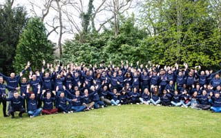 DataDome employees wearing blue DataDome sweatshirts stand in the grass surrounded by trees.