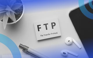 file transfer protocol (FTP) image of a post-it note pad with FTP file transfer protocol written on it. The note pad sits on a desk. A plant, a pair of airpods and a pen are also visible on the desk.