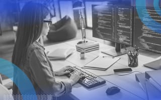 NPM woman with dark hair and glasses sitting at a desk and tying code into a computer