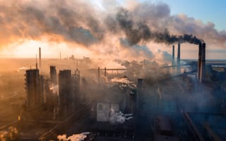 Smoke stacks releasing clouds of gas into the evening sky in an industrial setting.