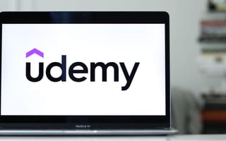 Udemy's logo on a laptop, resting on a gleaming desk.