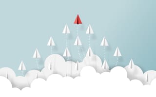 White paper airplanes follow a red paper airplane.