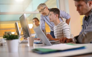 A mentor and apprentice work together at a desktop computer.