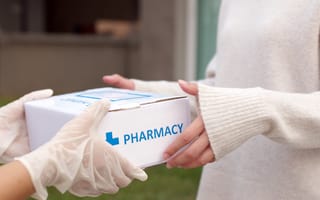 A delivery person hands a pharmacy package to a recipient.