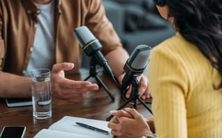 5 Top Podcast Companies Two hosts sit behind microphones recording a podcast.