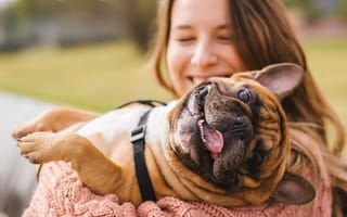 A woman holds a dog in her arms as the dog sticks its tongue out.