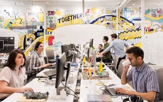 Photo of Zocdoc team members working at bench desk seating with wall full of graphic illustrations in background.