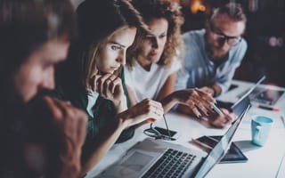 Four members of a mobile marketing team sit a desk gathered around a laptop.