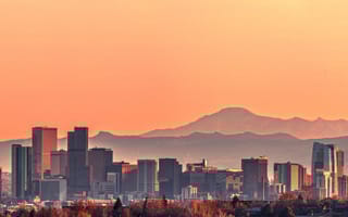 A photo of the Denver skyline, with mountains in the background, against an orange sky.