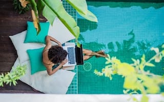 A person working with their laptop on their lap and feet in a pool.