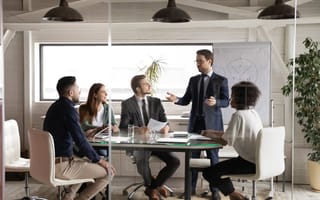 A group of five business people are gathered around a conference table discussing company vision.