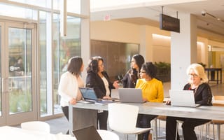 Five Liberty Mutual team members gather at a community table in Liberty Mutual’s common area with laptops, in discussion.