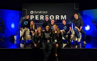 Nine Dynatrace team members sit on a stage with blue backlighting and a sign reading “Dynatrace Perform.”