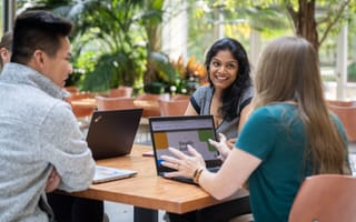 Three Workiva employees sit at an outdoor table with laptops in meeting, smiling.