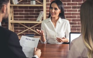 A job applicant talks to two interviewers across a desk. One of the interviewers holds a resume.