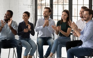A group of employees sit together clapping to represent employee recognition.