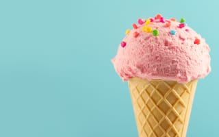 A pink ice cream cone with rainbow sprinkles on a mint green background.