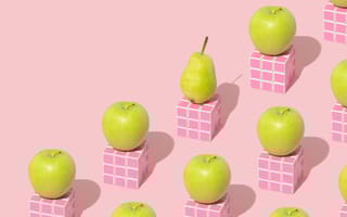 Bright green apples and pears rest on pink Rubix cubes in front of a pink backdrop.