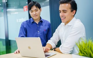 Two AlphaSights employees smile while looking at a laptop screen together.