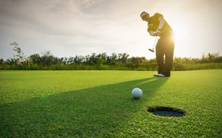 A golfer wearing a visor puts on a green.