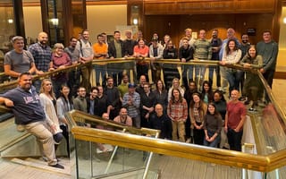 The Customer.io team gathers outside a ballroom entrance for a group photo on a stairway