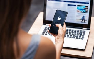 woman at computer looking at her phone which is prompting her for a code