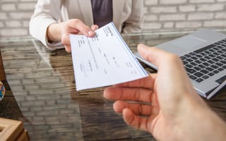 A close up of one hand passing a check to another hand over a desk to represent companies that pay well.