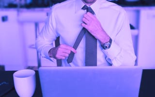 person adjusting neck tie and sitting down in front of laptop
