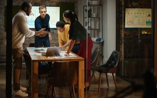 Want to Make an Outsized Impact? These Lean Teams Are Hiring A small team meeting in a conference room at night.