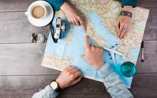 A close up of two pairs of hands pointing to a location on a world map.