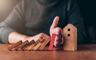 hand protecting house from falling dominoes