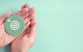two hands hold a paper cutout of an arrow hitting the center of a target