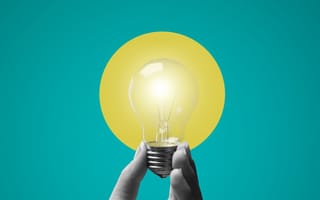 A hand holding a lit light bulb against a blue and yellow background