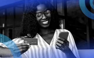 A smiling woman holding and looking at a smart phone and a credit card.