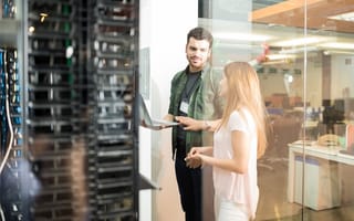 Two business people standing in server room with laptop and discussing something on the laptop.