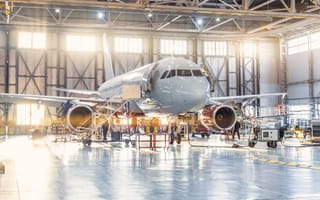 An aircraft sits in an aviation hanger as mechanics work on it.