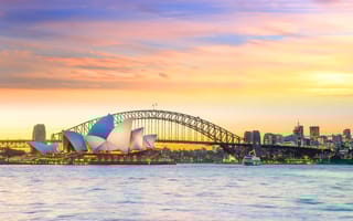 A view of the Sydney skyline at sunrise with the Sydney Opera House in the front and several tall buildings in the background.