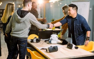 People shaking hands over a table with gaming consoles on them