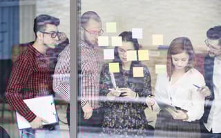 A group of coworkers look at sticky notes on a window.