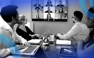 People in an office looking at colleagues who are on a video screen.