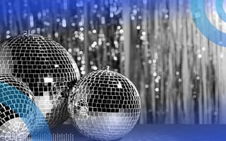 Three disco balls on a table in front of a wall covered in shiny tinsel.