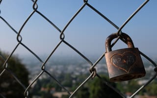 A padlock with a heart scratched on it connected to a chain link fence overlooking LA's Runyon Canyon.