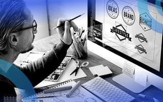 A man holding a pen pointing at logos he’s designing on a Mac computer.